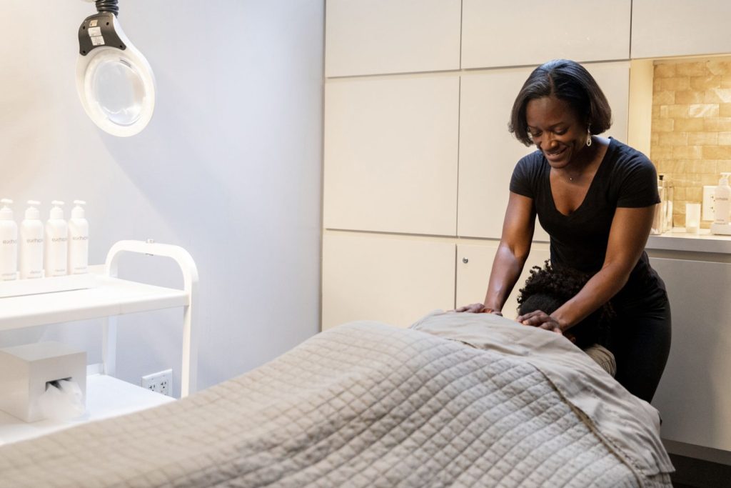A massage therapist smiling while she massages the shoulders of a woman lying on her table at the spa.